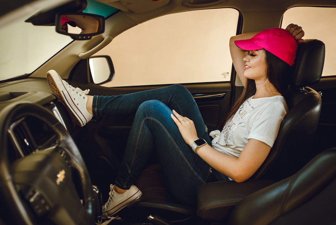 services-02 Woman in a car wearing a pink cap and jeans, smiling and relaxed.